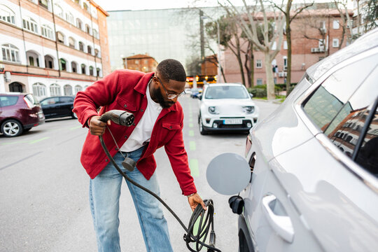 Man charging electric car on urban street during daytime
