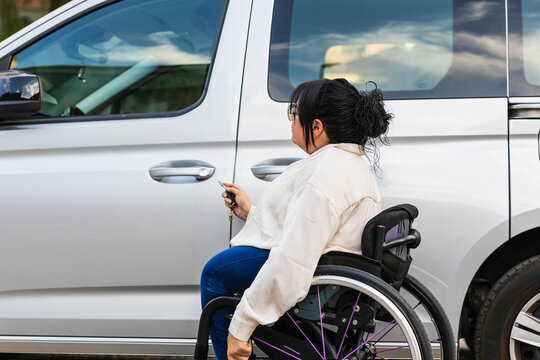 Woman using wheelchair unlocking adapted car in urban parking