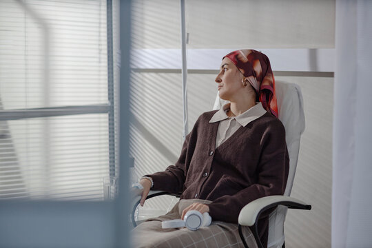 Patient receiving chemotherapy treatment in clinic room wearing headscarf