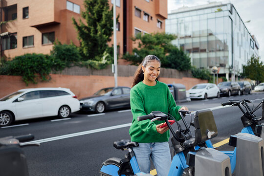 Woman unlocking bike share in city street for sustainable travel