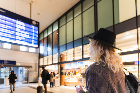 Young man waiting at train station checking schedule on smartphone