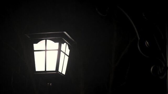 Close-up shot of a lit lantern with a six-paneled glass window in a dark setting with a warm glow.