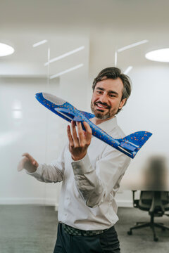 Businessman in office playing with airplane toy and smiling