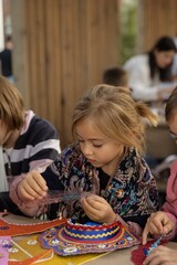 Fototapeta premium Girl creates craft with colorful patterns outdoors Description,Young girl concentrates on crafting activity, arranging colorful elements on decorative piece.