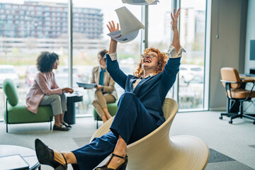Businesswoman celebrating success throwing papers in modern office lounge