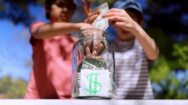Children learning financial responsibility by putting us dollar bills into a save jar, symbolizing early investment, savings for the future, and economic education