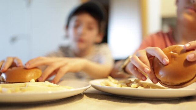 Two boys enjoying delicious hamburgers and french fries for lunch, a close-up on the plates of food with the hungry kids blurred in the background, representing a family meal
