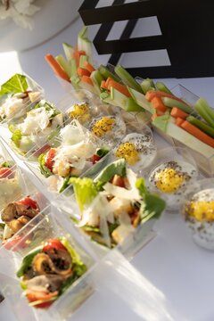 Assorted appetizers and snacks displayed on outdoor buffet table Description,Variety of finger foods including wraps, canap&eacute;s with olives and prosciutto, vegetable sticks, cheese cubes, and crispy sna