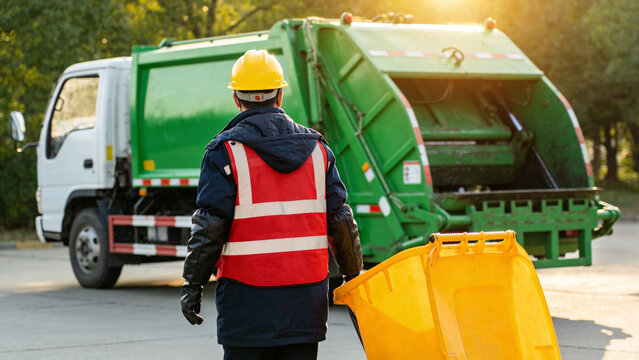 Worker collects waste in front of garbage truck during afternoon