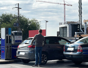 Llenar depósito de coche en gasolinera con manguera y gasolina de surtidor self service con precio por subida de barril de petróleo en guerra