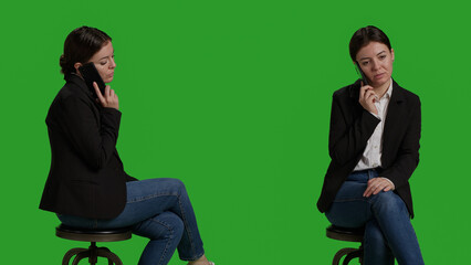 Fototapeta premium Close up of office worker talking on smartphone call over greenscreen background, using mobile phone and sitting on chair in studio. Young adult wearing formal suit on camera, telephone line.