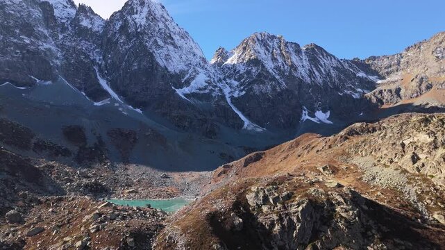 Zoom out revealing Chiaretto lake with turquoise water and dramatic Monviso peaks under clear sky.