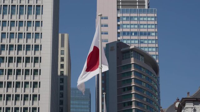 Japanese Hinomaru flag flying on pole between tall modern office towers in Tokyo central business district, clear blue sky