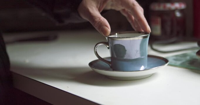 A man&rsquo;s fingers trace the gold rim of a tea cup in ambient low light. Excellent for mystery trailers, psychological thrillers, or creative storytelling about deep thought and waiting.