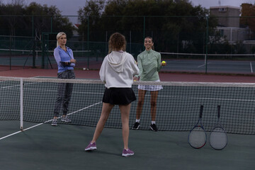 Obraz premium Female players practicing tennis at dusk on court, wearing hoodies, holding tennis ball and rackets