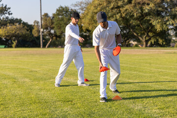Obraz premium Diverse male athletes practicing placing orange cones on sports field in white kit and black caps