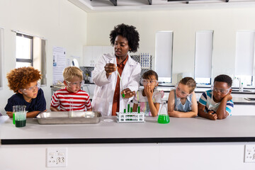 African American teacher guiding kids with goggles using pipette mixing green liquid at lab bench © wavebreak3