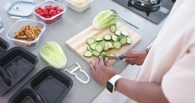 African American man slicing cucumber on kitchen board with knife, prepping black trays, copy space