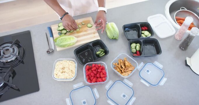 Adult male placing cutting board slicing cucumber prepping meals in black prep containers with rice