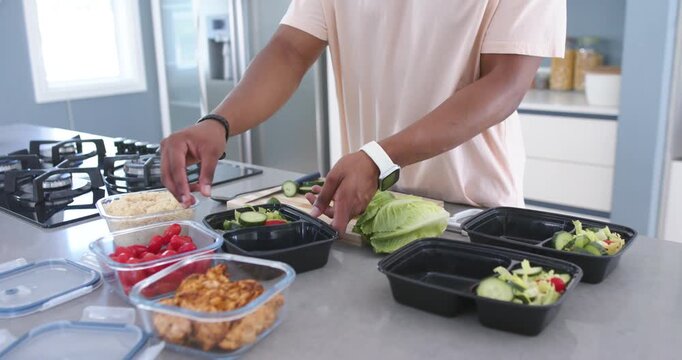 African American man assembling lunches at home starting with cucumbers into black boxes for lunch