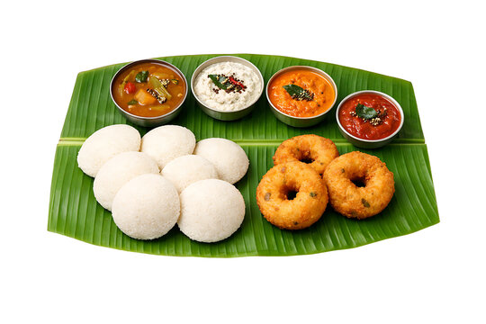 Traditional Indian vegetarian meal presentation featuring idli and medu vada with assorted chutneys and sambar in steel bowls on fresh banana leaf platter