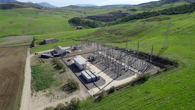 Electrical power station providing energy in a rural green valley with transmission towers and high voltage lines