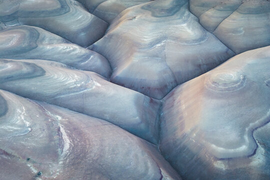 Aerial view of undulating, layered rock formations create a mesmerizing tapestry of pale blues, purples, and creams, carved by time and weather, Hanksville, Utah, United States.