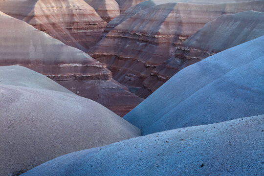 Aerial view of layered rock formations reveal earthy hues contrasting with cool blues, a geological tapestry woven across the landscape, Hanksville, Utah, United States.