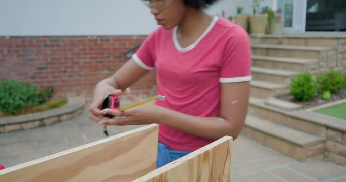 Adult African American woman measuring with tape, marking plywood on patio for cutting
