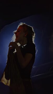 Vertical video: Concert singer flipping hair leaning into mic after flare rising, singing for crowd