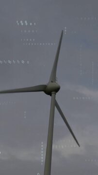 Vertical video: Wind turbine rotating from wind, generating power while binary overlaying blades