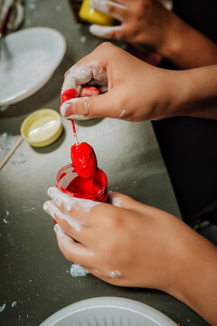 Close-up of hands dipping handmade sweets into red coating. Creative DIY craft process.