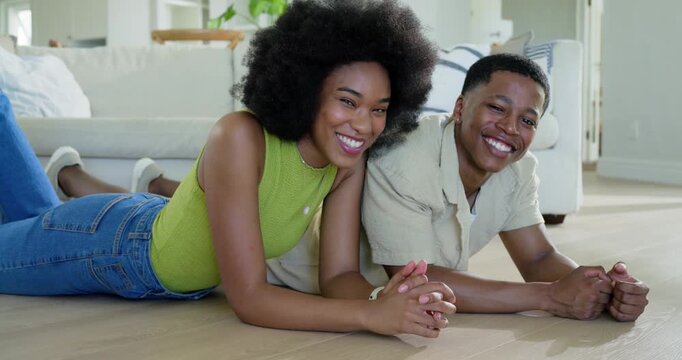 African American couple lying on wood living room floor near sofa, woman in lime-green top smiling