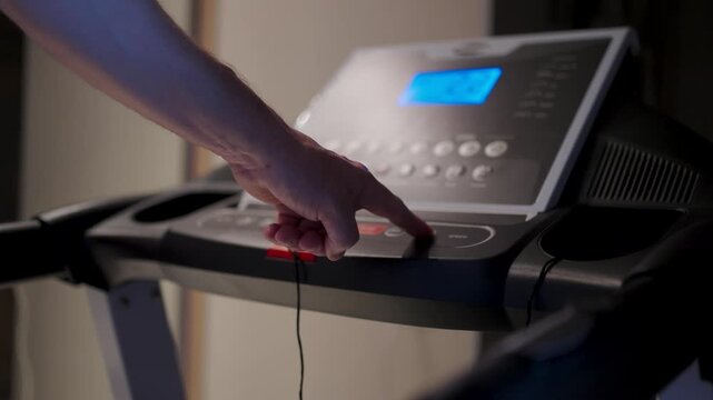 Man Hand Pressing Button on Treadmill Control Panel. Close-up of a person starting a workout by pressing a button on a treadmill dashboard. Modern cardio equipment in a home gym