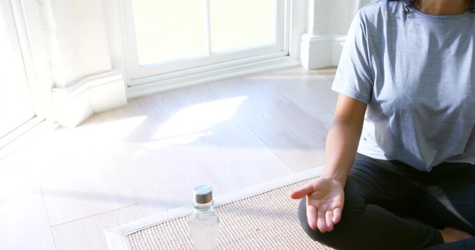 African American woman sitting on mat near bay window, picking headphones to meditate, copy space