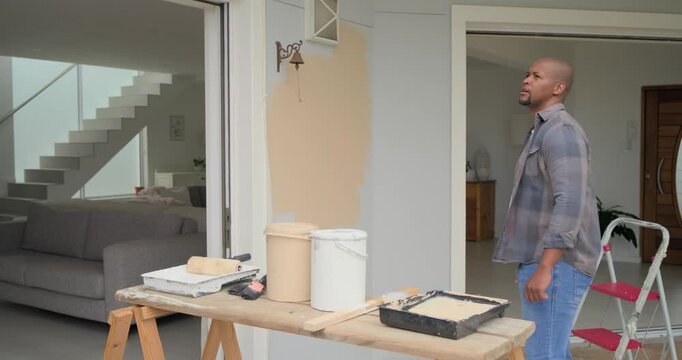 African man light-gray shirt seeing patch mixing beige paint with stir stick at doorway, copy space