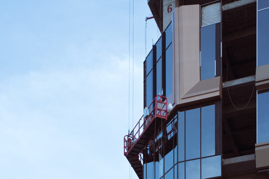 Construction workers installing glass panels from suspended scaffolding
