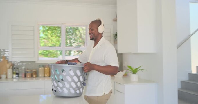 Adult African-American man with headset bringing laundry basket down to kitchen folding rust shirt