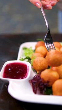 Soft donuts on a white square plate being pierced with a fork and dipped into vibrant red berry sauce. Close-up showing glossy texture and sweetness. 