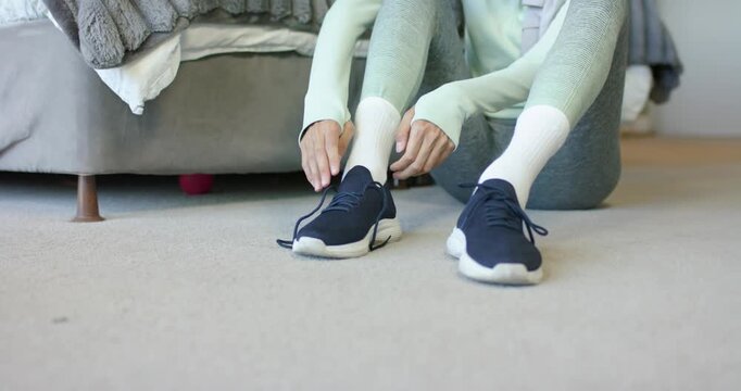 African American woman in activewear sitting by bed slipping into navy shoe lacing prepping for run