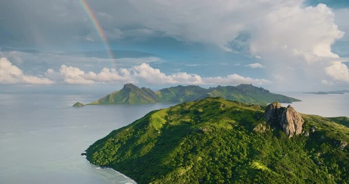 Yasawa Islands, Fiji: striking colorful rainbow arching over lush green volcanic mountains and pristine Pacific Ocean, revealing a tropical paradise nature landscape. Aerial view drone flight panorama
