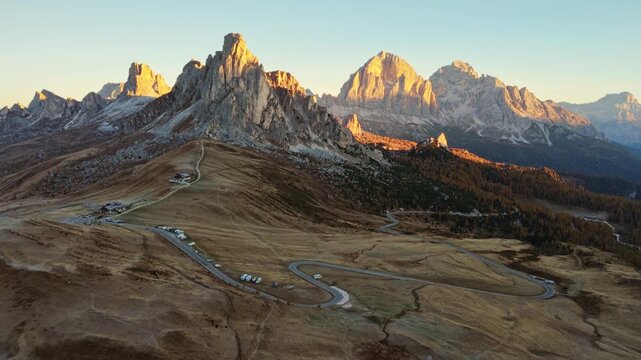 Golden sunrise over Passo Giau with Ra Gusela mountain peak, wooden lodge and winding road in Dolomites, Italy