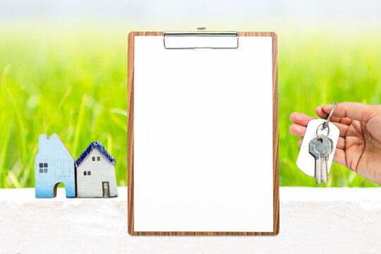 Blank report paper on wooden clipboard with miniature house and house key over blurred green grass, property investment and real estate business