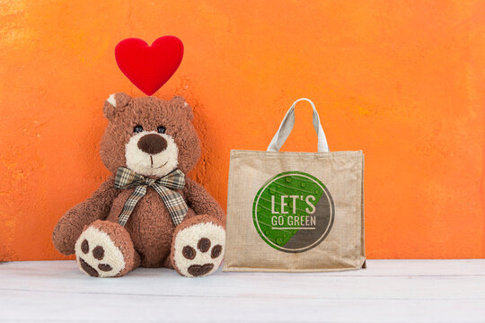 Lets' go green logo on grocery bag with old teddy bear sitting on orange cement wall background, environmental friendly concept
