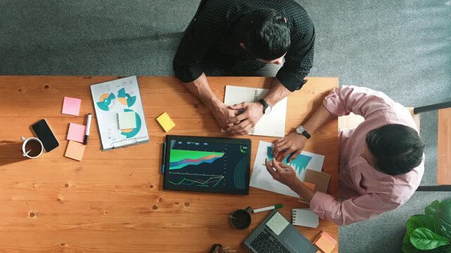 Top view of skilled project manager talking about financial graph to investors while sitting at meeting table with data analysis document. Diverse team discussing and brainstorming idea. Convocation.
