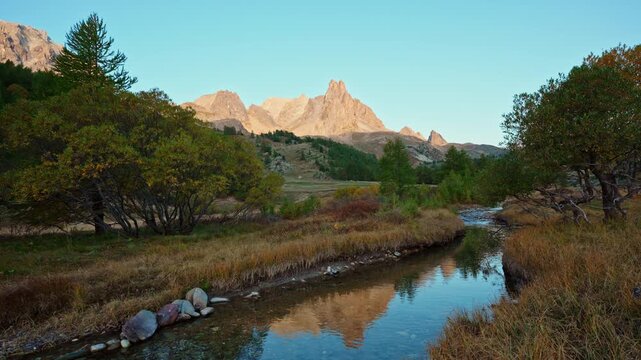 Scenic landscape of Claree Valley with Main De Crepin peak with river flow through in autumn forest at French Alps, France