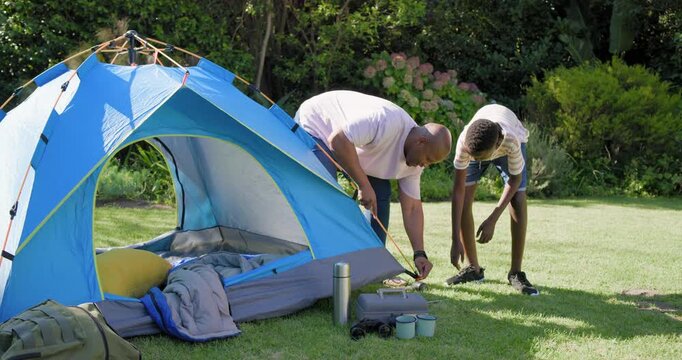 African father and boy checking tent guy line, securing stake with mallet to anchor backyard camp