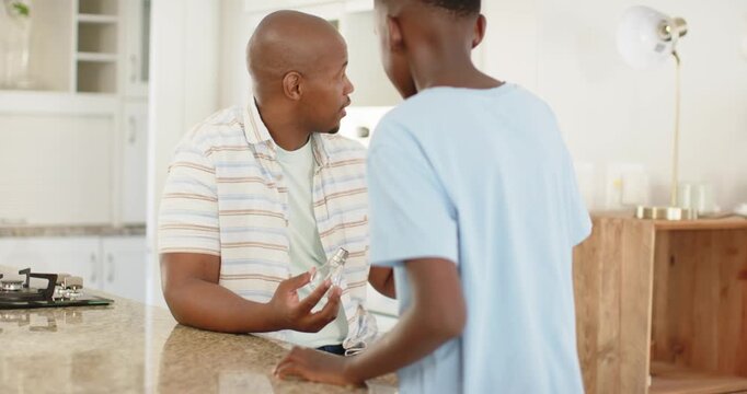 Father and son at kitchen island, father showing clear bottle, explaining, son leaning in listening