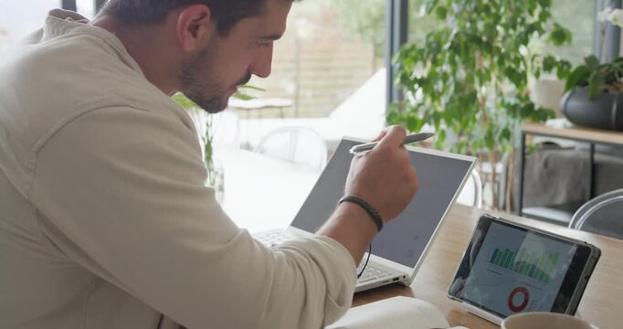 Man noticing charts on tablet, leaning, picking stylus, tapping, writing notes at home table