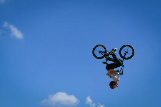 Chichester, United Kingdom - 14 July 2018: View of a BMX rider executing a daring mid-air flip against a backdrop of clear blue skies and scattered clouds at Goodwood Motor Circuit.